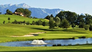 A golf course with a pond, trees, and mountains in the background. - Stylish loft with a great panoramic view (Veysonnaz)