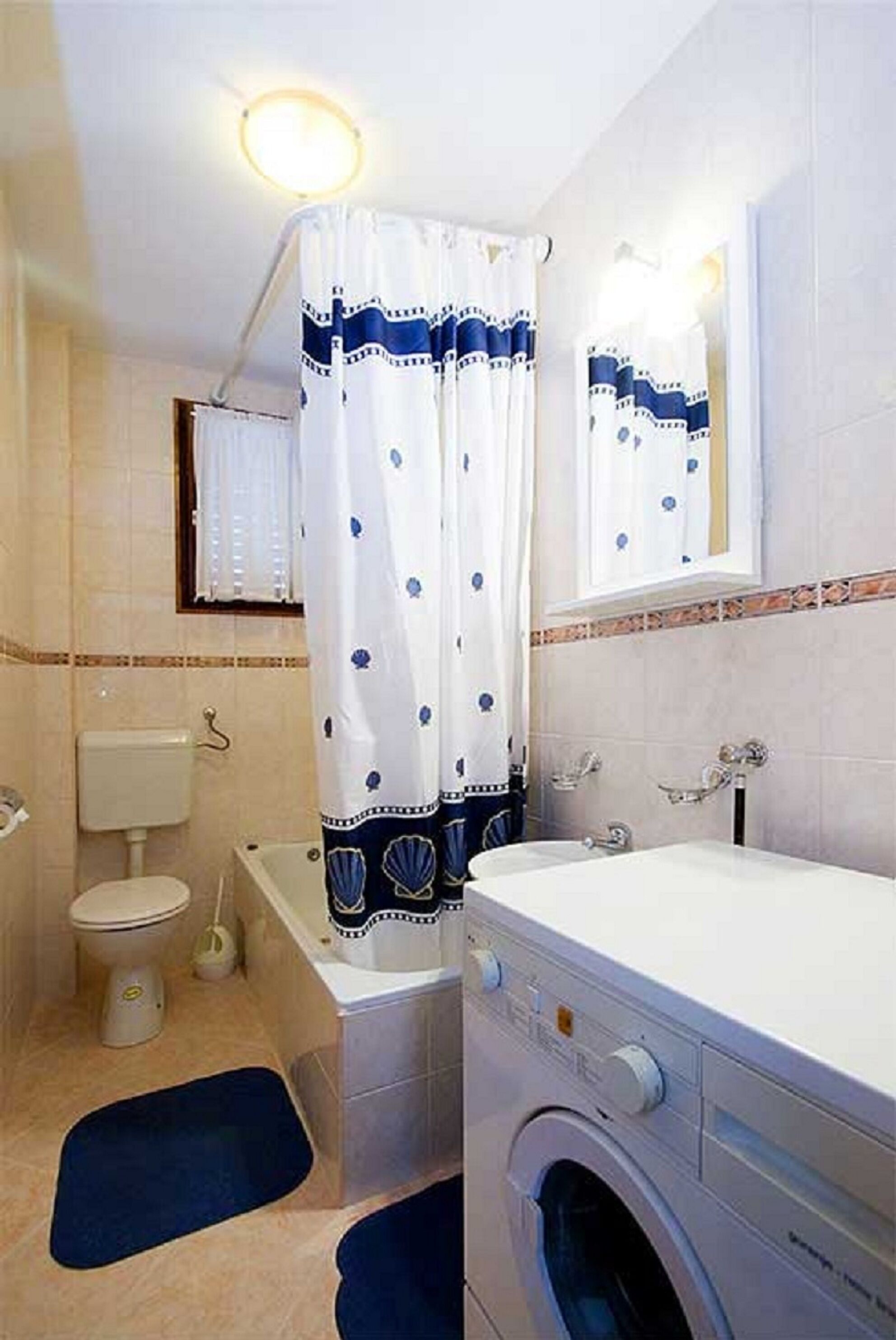Une petite salle de bain comprenant des toilettes, une baignoire et un lave-linge.
