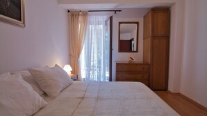 Un dormitorio con cama, mesita de noche, cómoda, espejo y ventana con cortinas.