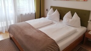 Un lit bien fait, avec du linge de lit blanc et des oreillers, une tête de lit recouverte d’un tissu vert et une œuvre d’art florale accrochée au mur.