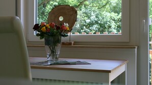 Una ventana con un adorno de madera, un florero con flores y una mesa con una revista.