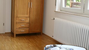 Una habitación con un armario de madera, un televisor de pantalla plana, una mesa blanca con revistas y una ventana con vistas a árboles.