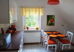 Una cocina con comedor, una ventana con cortinas, un radiador y un microondas.