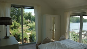 A bedroom with a large bed, a wardrobe, and a view of a lake and greenery. - Lakeside new direct lakeside location lakeside terrace, bathing lake, biosphere wifi (salem)