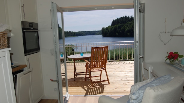 An open door leading to a balcony with a table and chairs, overlooking a lake. - Lakeside new direct lakeside location lakeside terrace, bathing lake, biosphere wifi (salem)