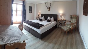A bedroom with a bed, bedside tables, a chair, a table, and a deer skull on the wall.