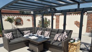 A covered outdoor seating area with a sectional sofa, a table, and a lantern.