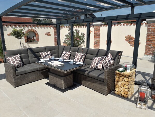 A covered outdoor seating area with a sectional sofa, a table, and a lantern.