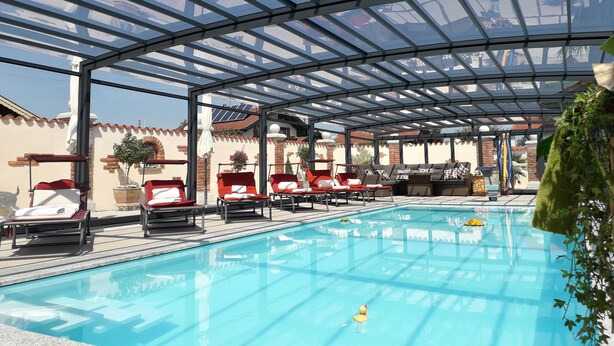 A covered swimming pool with lounge chairs and a glass ceiling.