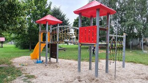 A playground with a slide, climbing structures, and a red-roofed playhouse.