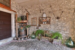 Paredes de pedra rústicas com uma porta de madeira, uma prateleira de madeira com vasos e um candeeiro pendente.