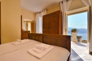 Quarto de hotel com duas camas, cabeceira de madeira, um espelho grande e varanda com vista para o mar.