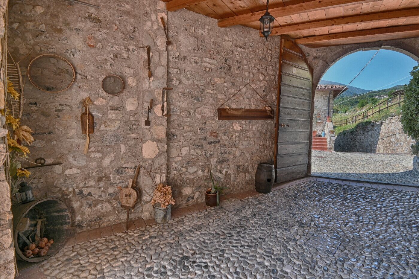 Une pièce rustique aux murs de pierre, dotée d’une porte en bois, d’une lanterne suspendue et d’un sol en pierre.