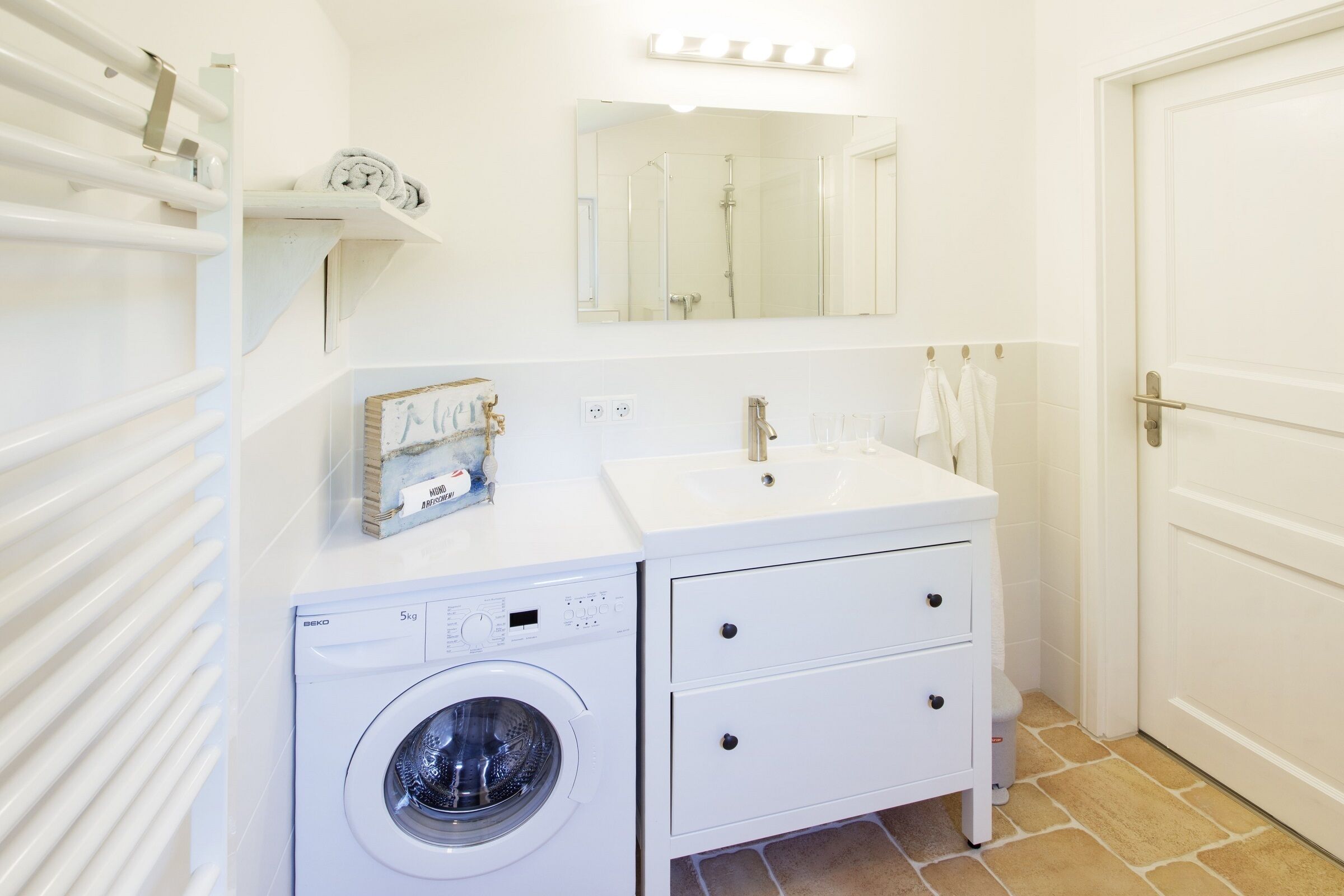 Een badkamer met een wasmachine, een wastafel, een spiegel en een handdoekrek.