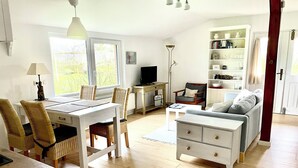 A well-lit living room with a dining area, a sofa, a TV, and a bookshelf. - Hühnerstall -Shower, terrace, beach chair, sauna, near the beach, child-friendly (Pugholz)