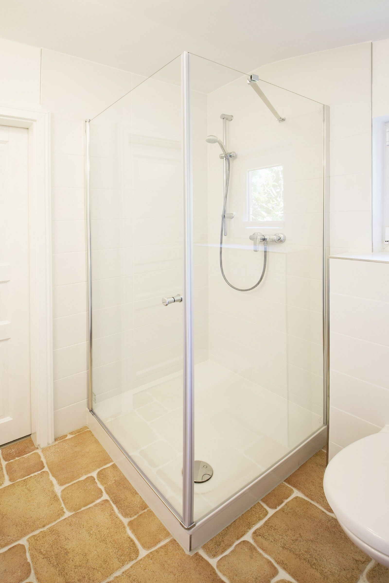 A glass-enclosed shower with a handheld showerhead and a handheld faucet.