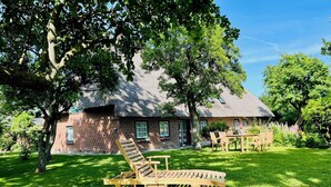 A rustic brick house with a thatched roof, surrounded by a well-maintained lawn and trees. - Hühnerstall -Shower, terrace, beach chair, sauna, near the beach, child-friendly (Pugholz)