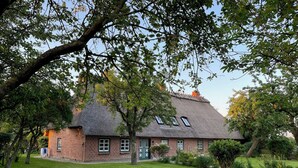 A traditional brick house with a thatched roof, surrounded by a well-maintained lawn and mature trees. - Hühnerstall -Shower, terrace, beach chair, sauna, near the beach, child-friendly (Pugholz)