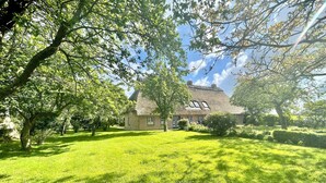 A traditional house with a thatched roof, surrounded by a well-maintained lawn and mature trees. - Hühnerstall -Shower, terrace, beach chair, sauna, near the beach, child-friendly (Pugholz)