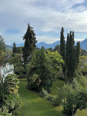 A lush garden with a variety of trees and a white building with green roofs. - stylish, sunny, and quiet penthouse with a dream view - relax and enjoy (Meran)