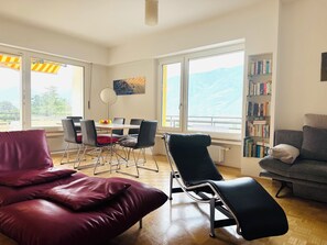 A modern living room with a dining area, large windows, and a bookshelf.