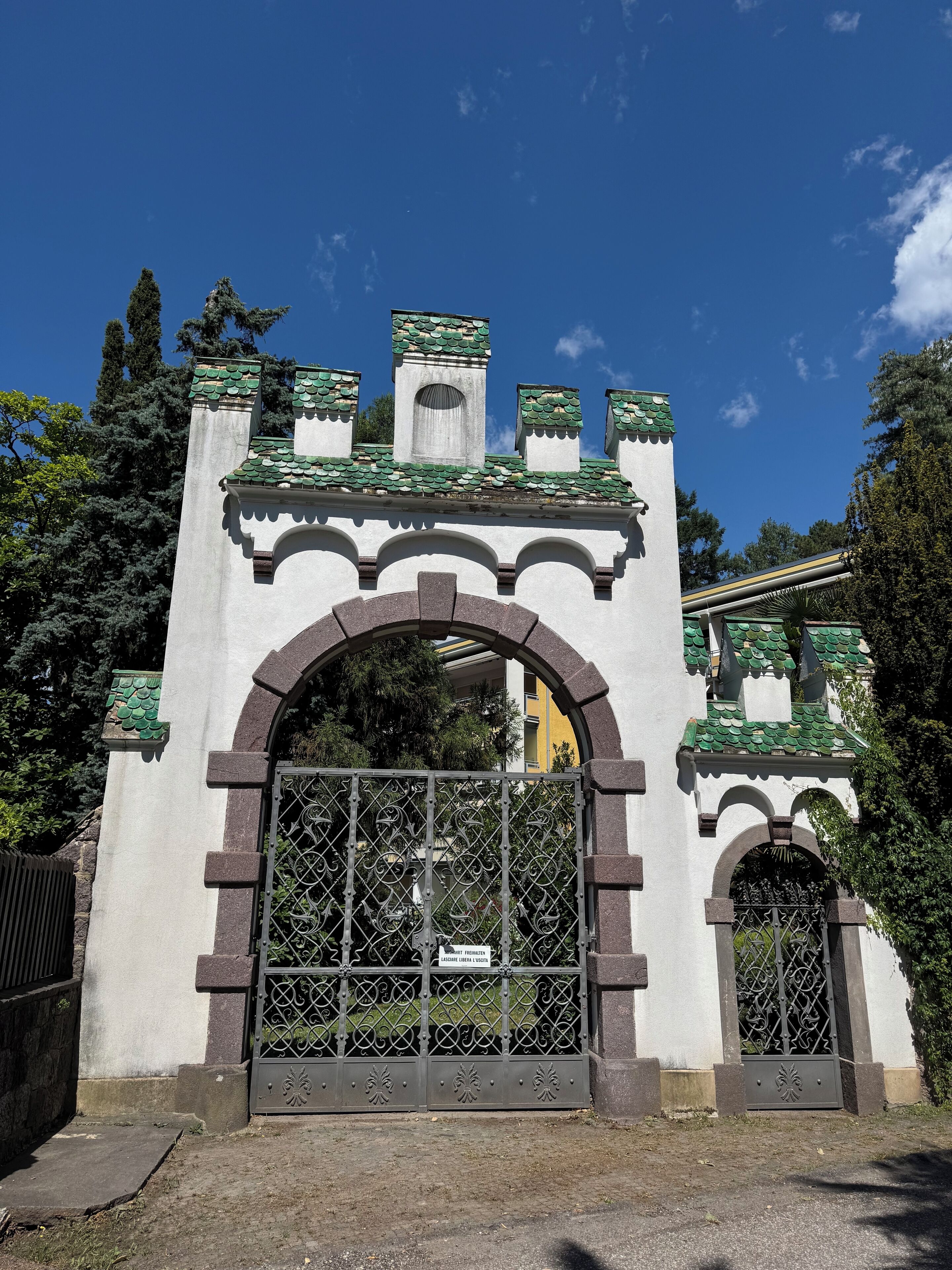 Une entrée fermée par un portail, agrémentée d’une arche décorative et d’une grille en métal.