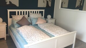 A bedroom with a white bed, floral bedding, and artwork on the walls. - NEW! Modern 3-room apartment in Lüneburg, close to the city, quiet, outskirts (Lüneburg)
