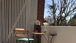 A small outdoor patio with a wooden floor, two chairs, a table, and a potted plant. - NEW! Modern 3-room apartment in Lüneburg, close to the city, quiet, outskirts (Lüneburg)