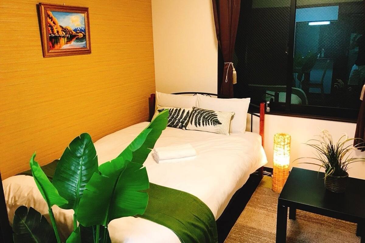 Une chambre d’hôtel avec un lit, une table de chevet, une lampe, une plante et un tableau au mur.
