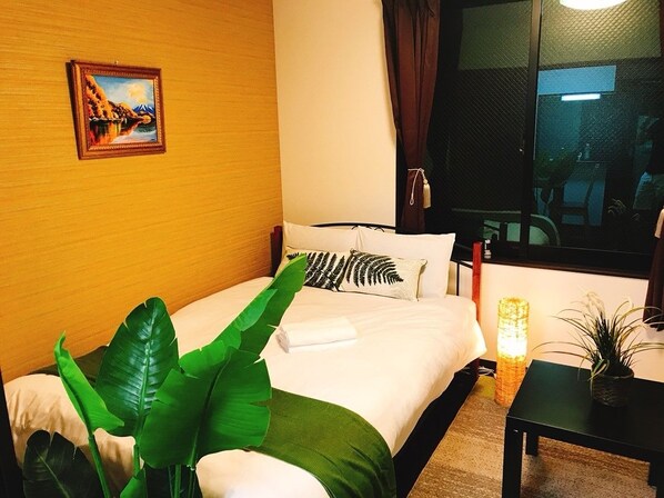 A hotel room with a bed, a nightstand, a lamp, a plant, and a painting on the wall.