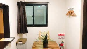 A small room with a wooden table, a potted plant, a window with curtains, a fire extinguisher, and a coat rack. - GH One More Heart at Kamishichiken 3 (Kyoto)