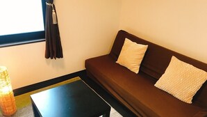 A room with a brown sofa, two pillows, a black table, and a window with curtains. - GH One More Heart at Kamishichiken 3 (Kyoto)