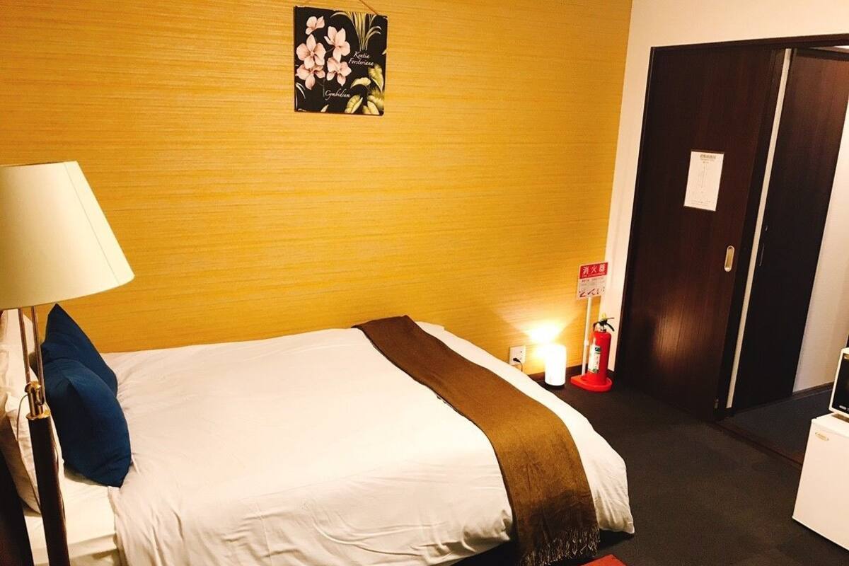 Une chambre d’hôtel avec un lit, une table de chevet avec une lampe, une horloge murale et une porte.