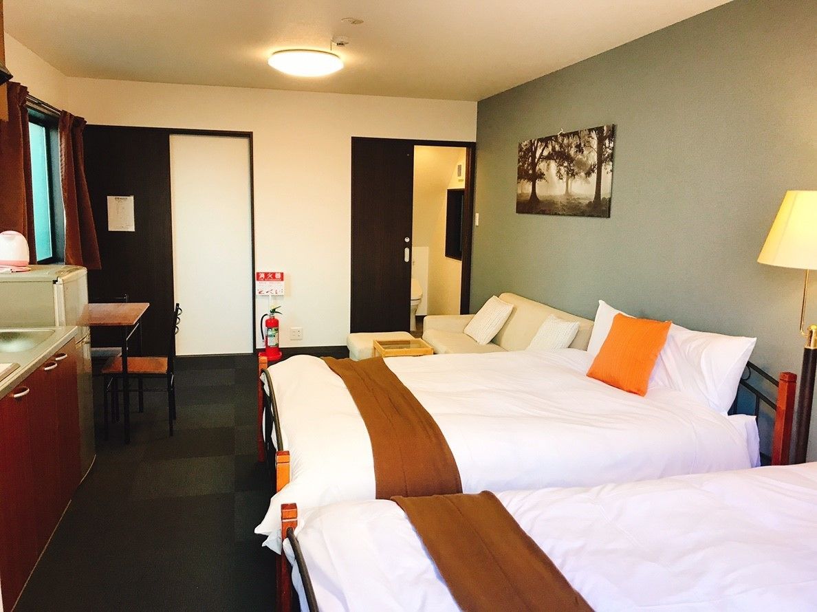 A hotel room with two beds, a desk, a chair, a lamp, and a painting on the wall.