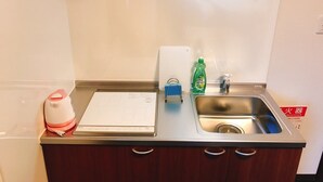 Une petite cuisine équipée d’un évier en acier inoxydable, d’une bouilloire, d’un flacon de liquide vaisselle et d’un bloc-notes posé sur le comptoir.