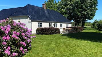 Une maison blanche avec un toit foncé, entourée d’une pelouse bien entretenue et d’un grand arbre.