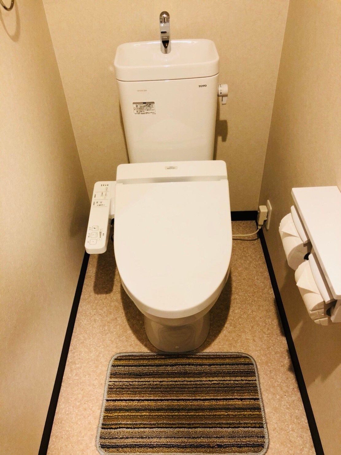 A small, compact bathroom with a toilet, bidet, and a control panel.