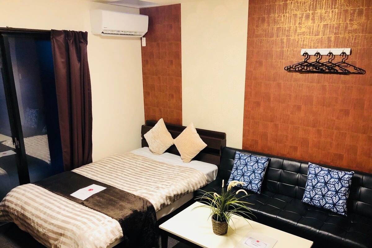 A hotel room with a bed, a sofa, a coffee table, and a wall-mounted air conditioner.