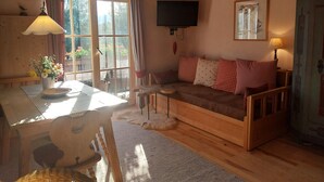 A cozy room with a wooden ceiling, a sofa with patterned cushions, a television mounted on the wall, and a dining table with a lamp. - Heissbauer - Cozy "Obstgarten" Vacation Rental with Mountain Views - Ideal for Families (Wackersberg)