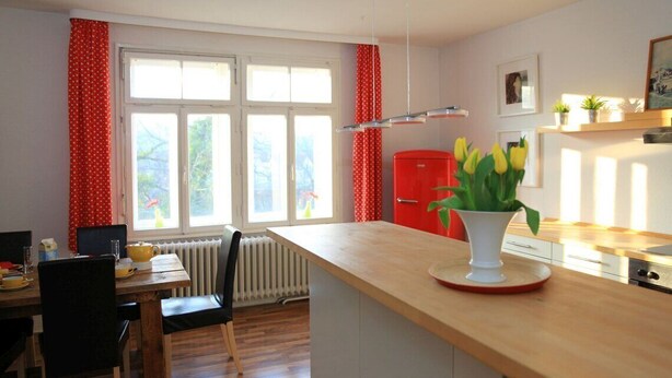A kitchen with a wooden countertop, a red refrigerator, and a window with red curtains.