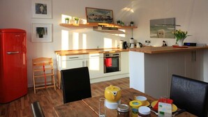 A compact kitchen with a red refrigerator, wooden countertops, and a dining table set with yellow and red dishes.