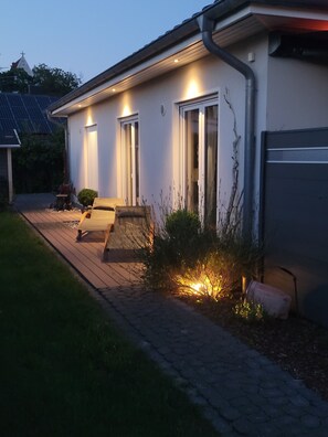 Uma casa com um caminho de acesso pavimentado, um banco e uma pequena área de jardim com plantas.