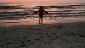 Une personne se tient sur une plage, face à l’océan, au moment du coucher du soleil.