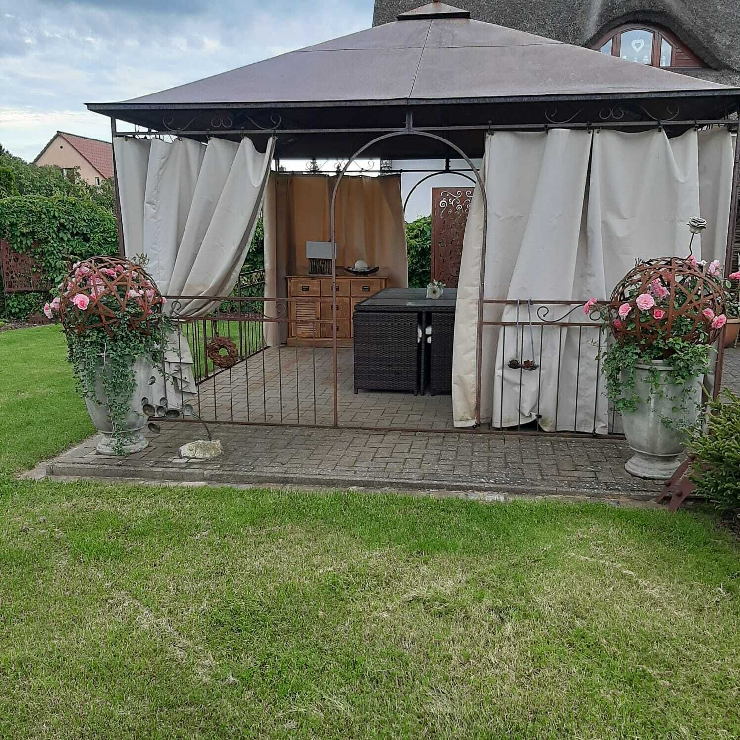 Ein Gartenpavillon mit einem gefliesten Patio, einem Holzkabinett und zwei großen Blumentöpfen.