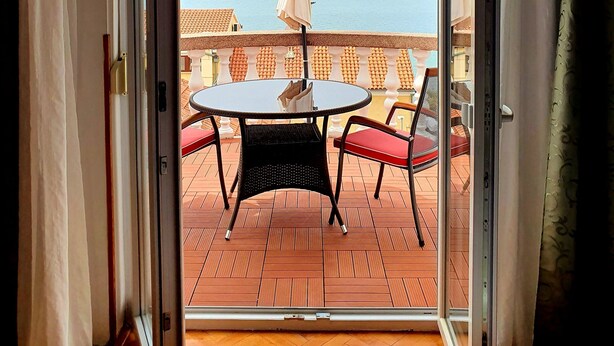 A room with a sliding glass door leading to an outdoor terrace with a table and chairs, an umbrella, and a view of the sea. - MODERN APARTMAN - 4 TO 6 PERSONS WITH A STUNNING SEA VIEW (TISNO)