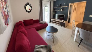 A modern living room with a red sofa, a TV, a ceiling fan, and a dining area. - MODERN APARTMAN - 4 TO 6 PERSONS WITH A STUNNING SEA VIEW (TISNO)