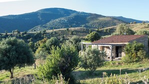 Une maison en pierre avec un toit de tuiles, entourée de verdure et de collines.