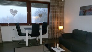 Olohuoneessa on tummanvärinen sohva, lasinen sohvapöytä sekä ruokailutila, jossa on kaksi tuolia ja pöytä.