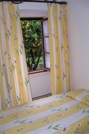 A bedroom with a bed, yellow floral curtains, and a window with a view of a tree and a building. - Very central and quiet apartment for two people (Sintra)