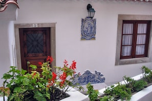 A building facade with a numbered door, a decorative wall-mounted light fixture, and a window with curtains. - Very central and quiet apartment for two people (Sintra)